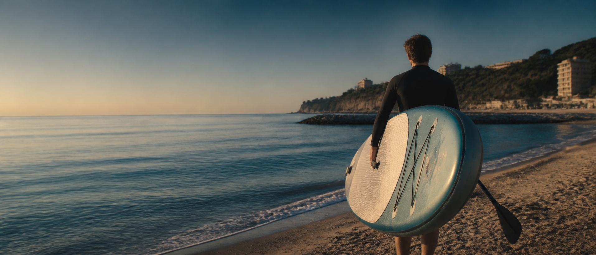 Una persona porta il proprio SUP verso il mare al mattino