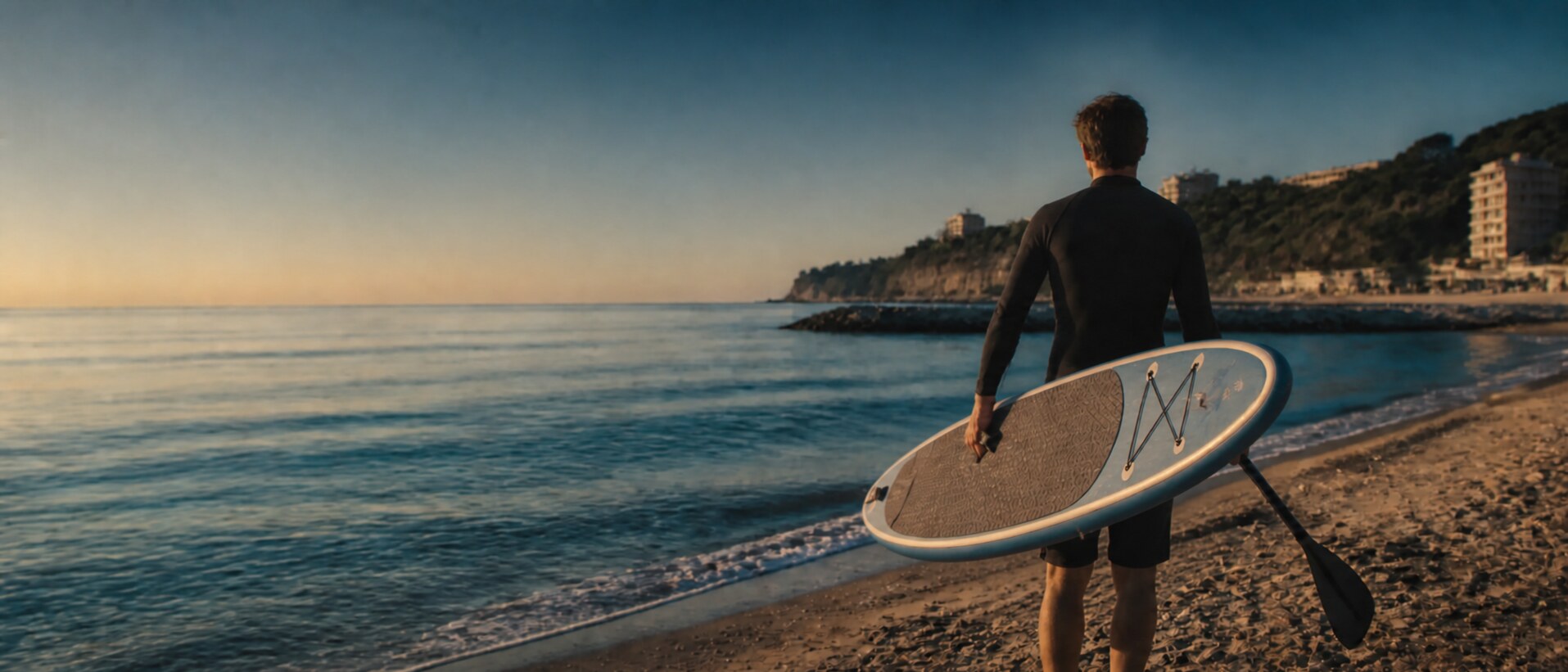 Una persona porta il proprio SUP verso il mare al mattino
